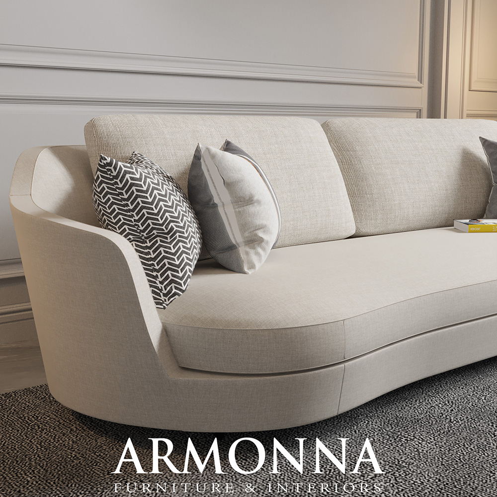 Beige curved sofa with two light cushions and a black-and-white zigzag pillow on a textured rug.