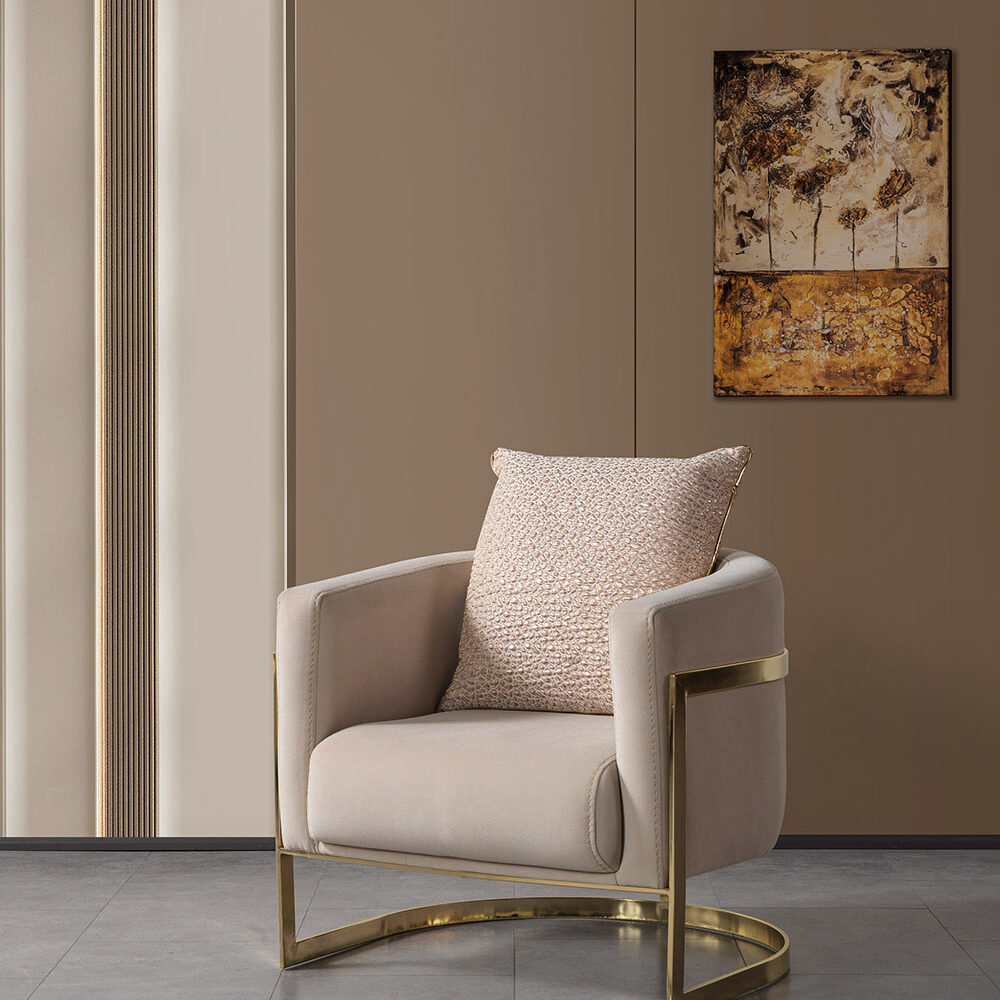 Beige upholstered armchair with a gold metal frame and a textured pillow, in a neutral living room with wall art.