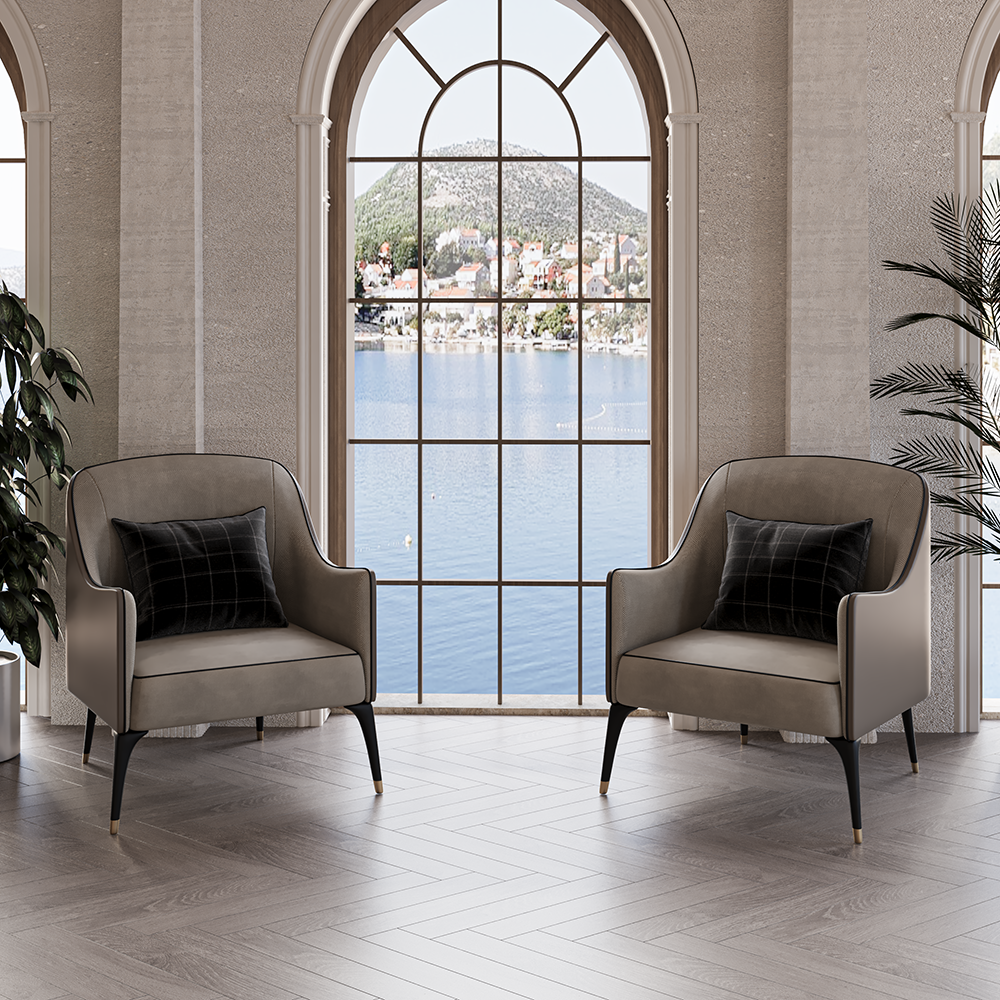 Pair of taupe armchairs with black pillows facing a large arched window overlooking a lake and hillside village, creating a cozy living room scene.