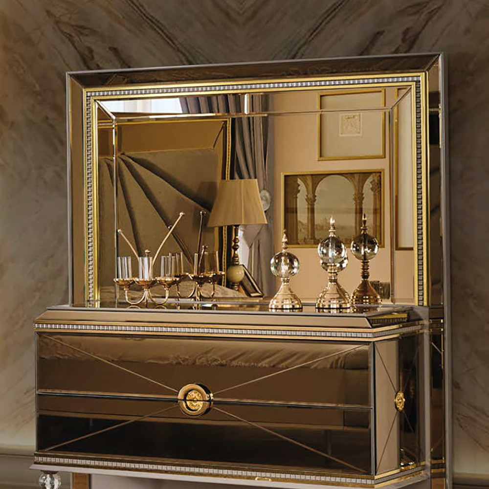 Luxurious gold and mirrored dresser with a large framed mirror, crystal decanters, and candlesticks in a marble-walled room.