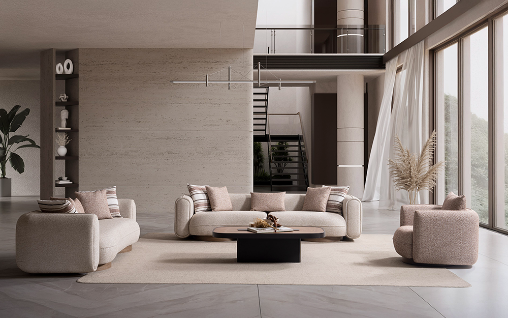 Open, airy living room with beige sectional sofas around a round coffee table on a pale rug; floor-to-ceiling windows and a staircase in the background.