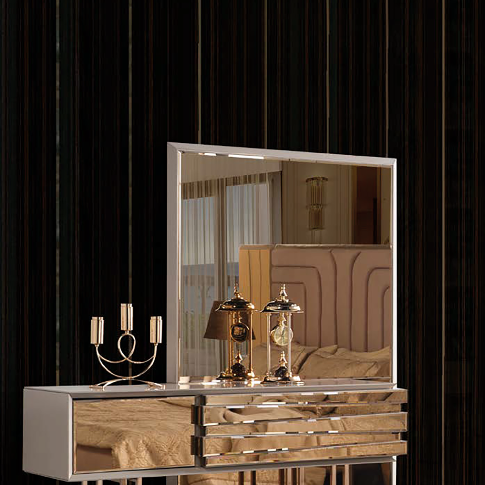 Modern mirrored vanity table with gold accents and a large rectangular mirror, topped with candelabra and lanterns; reflection shows a bedroom with a tufted headboard.