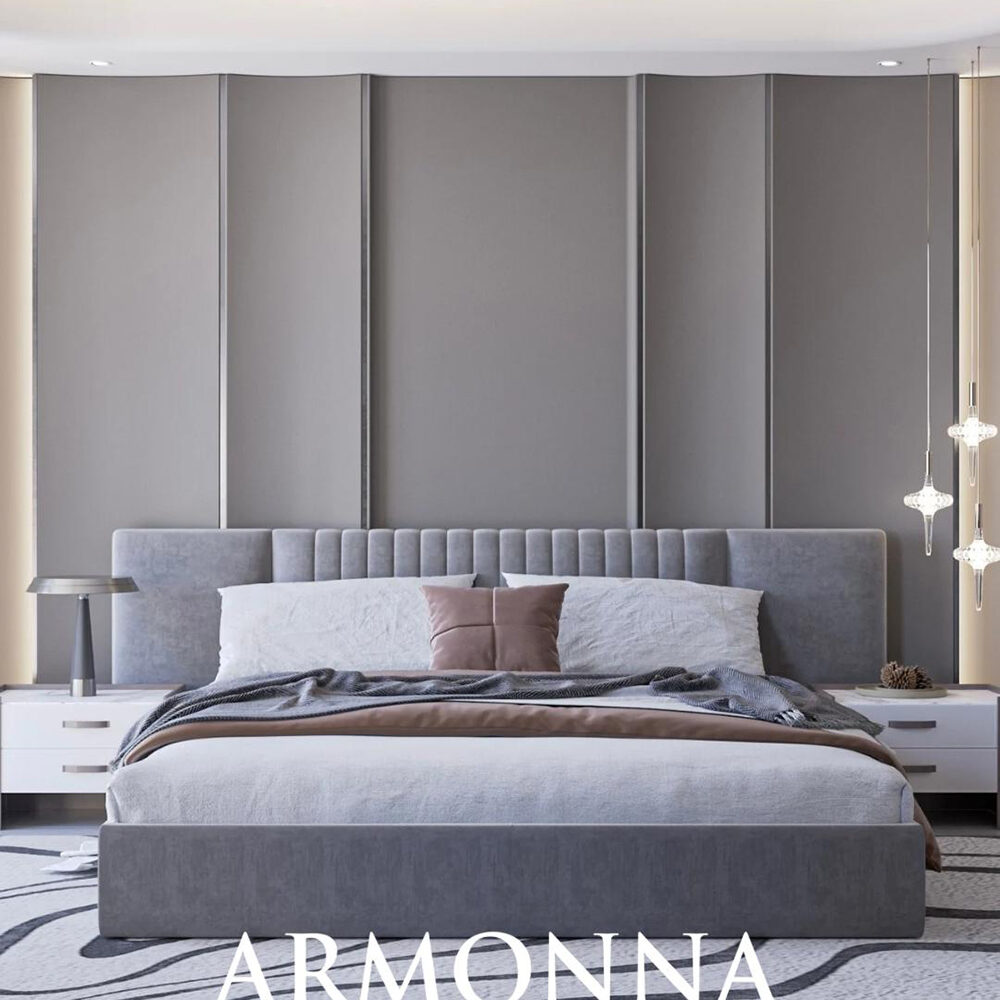 Gray upholstered king bed with a tall paneled headboard in a modern, neutral-toned bedroom with side tables and pendant lights, ARMONNA branding visible at the foot of the bed.