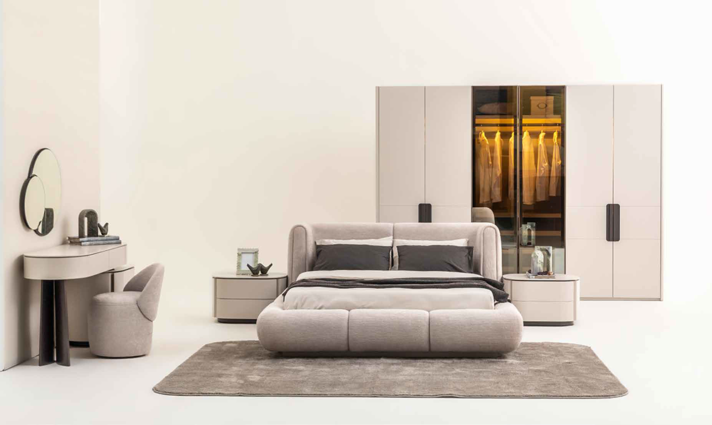 Modern bedroom with a plush gray upholstered bed, matching nightstands, and a large wardrobe in neutral tones.