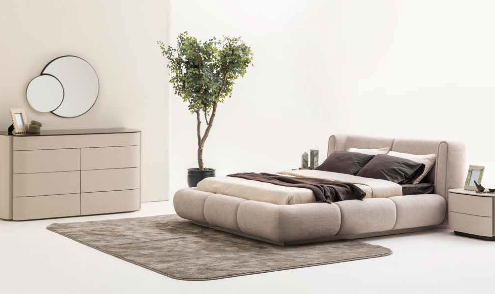 Neutral beige bedroom with a low, upholstered bed, matching nightstands, and a dresser with dual round mirrors on the wall.