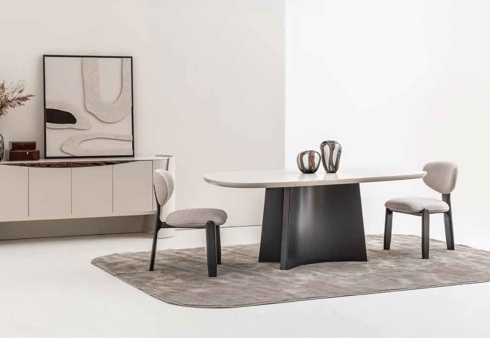 Minimalist dining area with an oval white table, two padded chairs, a gray rug, and a sideboard with framed abstract art.