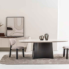 Minimalist dining room oval white table on a dark pedestal base two gray upholstered chairs and a neutral rug