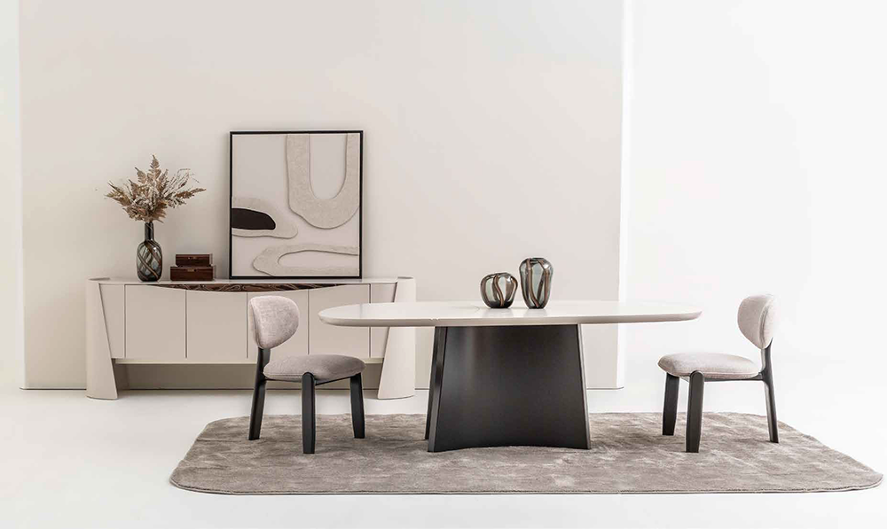 Minimalist dining room: oval white table on a dark pedestal base, two gray upholstered chairs, and a neutral rug.