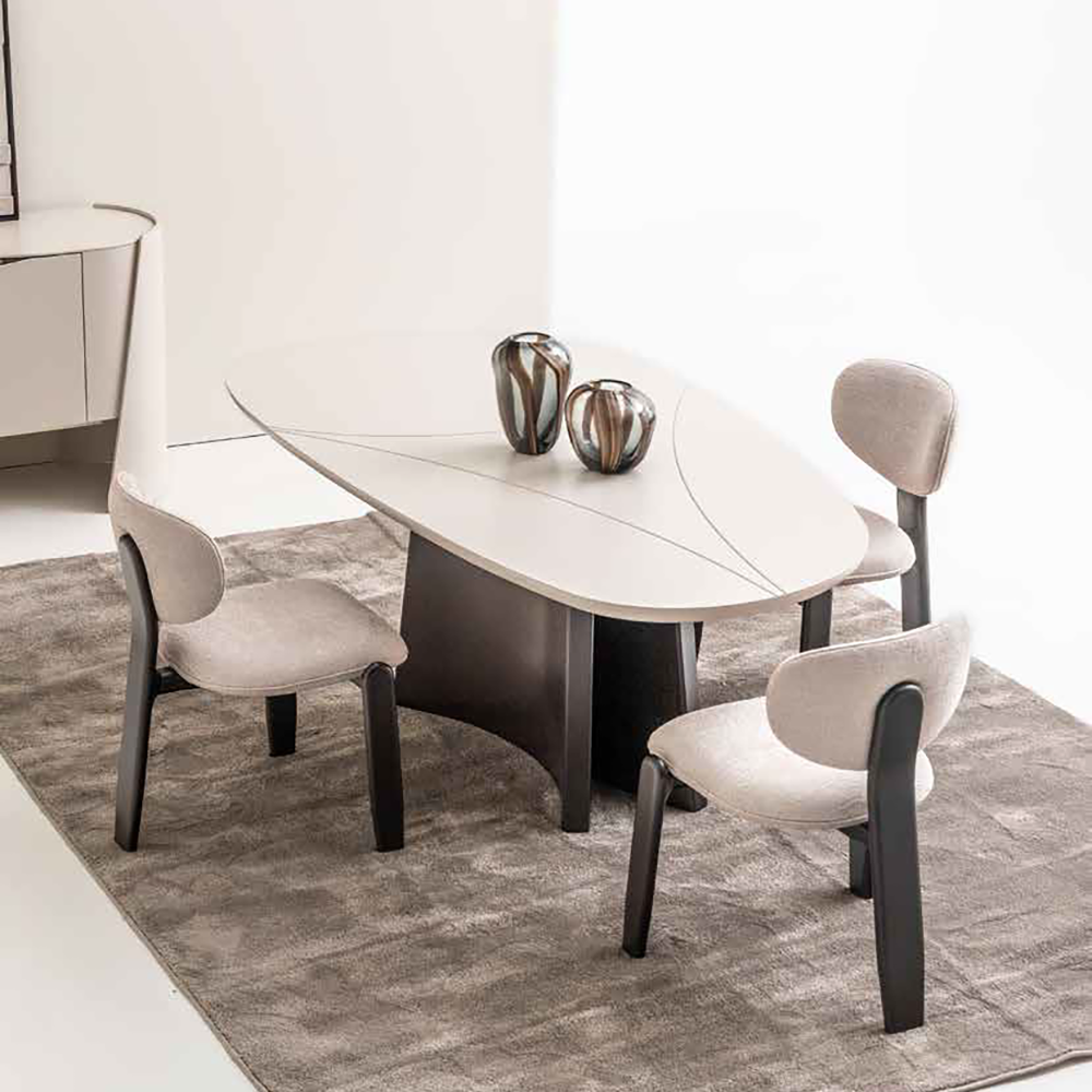 Contemporary dining set: oval beige table with dark pedestal, three beige upholstered chairs, two decorative vases on the table.