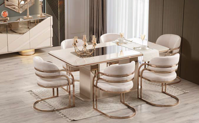 Elegant dining room scene with a white glossy table, six cream upholstered chairs with gold metal frames, and a candle centerpiece.