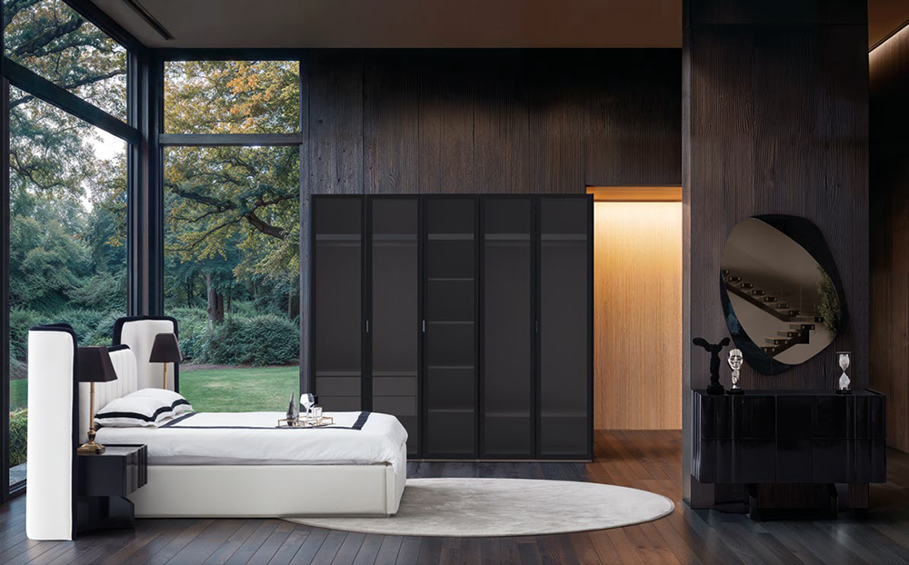 Modern bedroom with dark wood walls, large windows, a white bed, and a black wardrobe set against a circular rug.