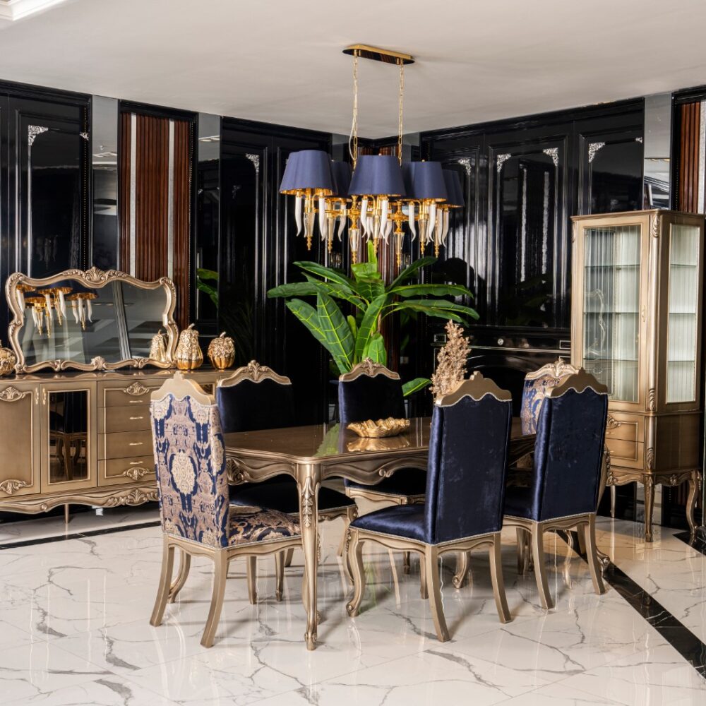 Luxurious dining room with gold ornate furniture, blue velvet chairs, and a crystal chandelier in a showroom setting.