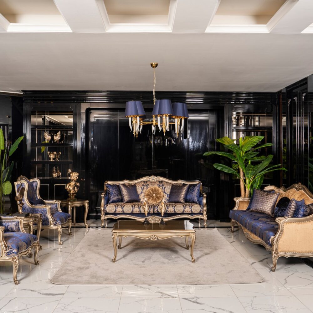 Luxurious living room with blue and gold upholstered sofas and chairs, marble floor, and a gold-accented coffee table under a blue chandelier.