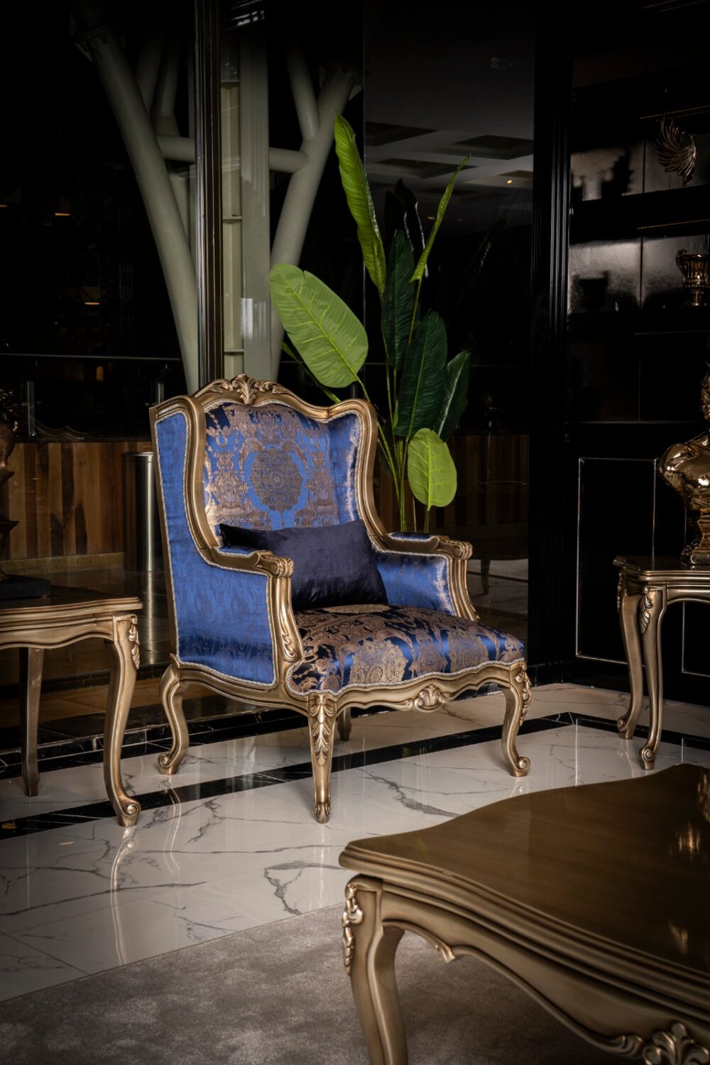 Emirgan Classic Set 38 Armonna Elegant blue and gold damask armchair with carved frame in a luxe indoor setting next to a tall green plant and marble floor