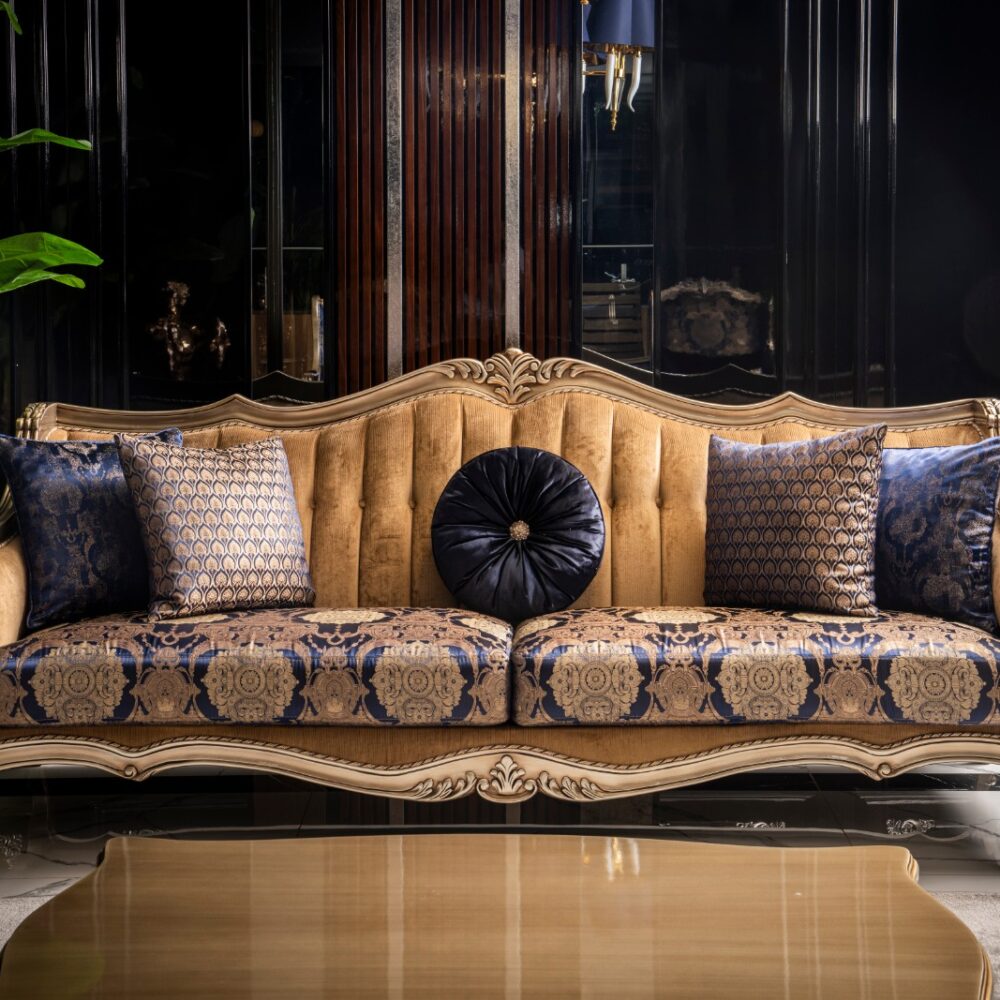 Luxurious gold-framed sofa with tufted beige upholstery and blue damask cushions in an upscale living room.