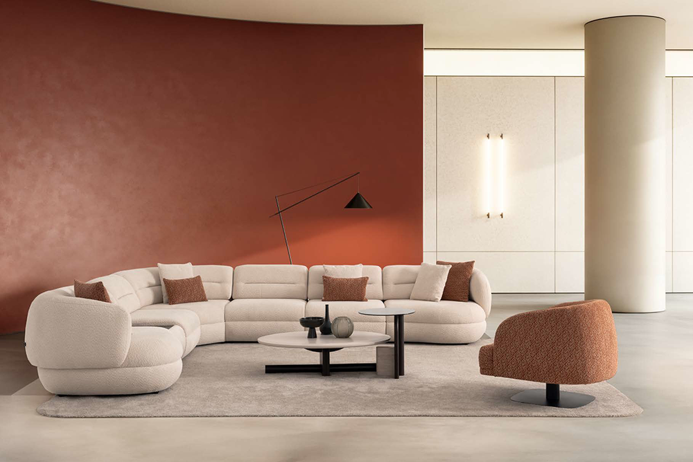 Modern living room with a curved off-white sectional sofa, rust accent wall, and round coffee tables on a light rug.