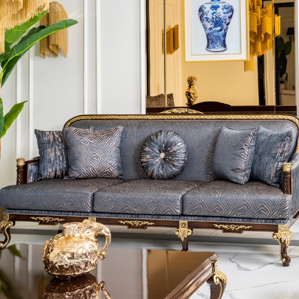 Luxurious living room with a blue patterned sofa framed in gold, plush cushions, and a tall green plant nearby.
