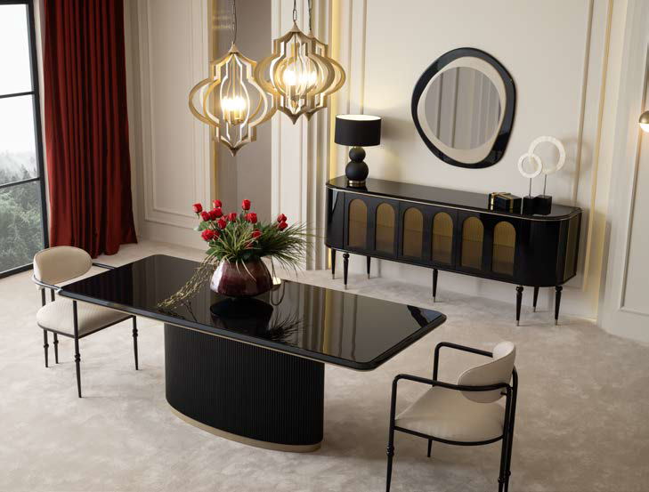 Luxurious black-gloss dining table in a chic modern room with sculptural pendant lights and a sideboard with a round mirror above it, vase of red flowers centerpiece.
