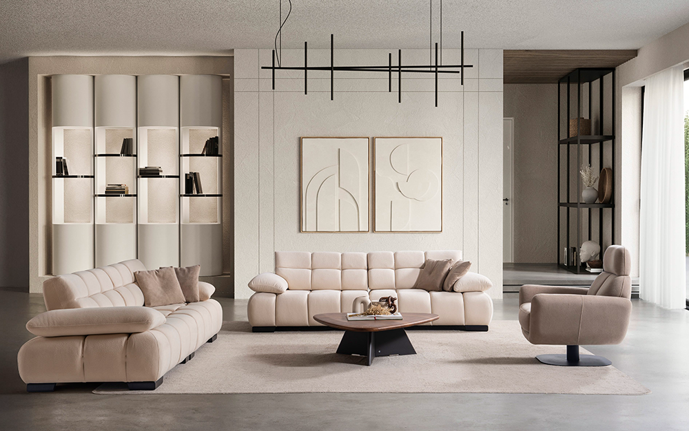 Modern living room with pale pink sectional sofas around a circular coffee table on a beige rug, abstract art on the wall and a black geometric chandelier above.