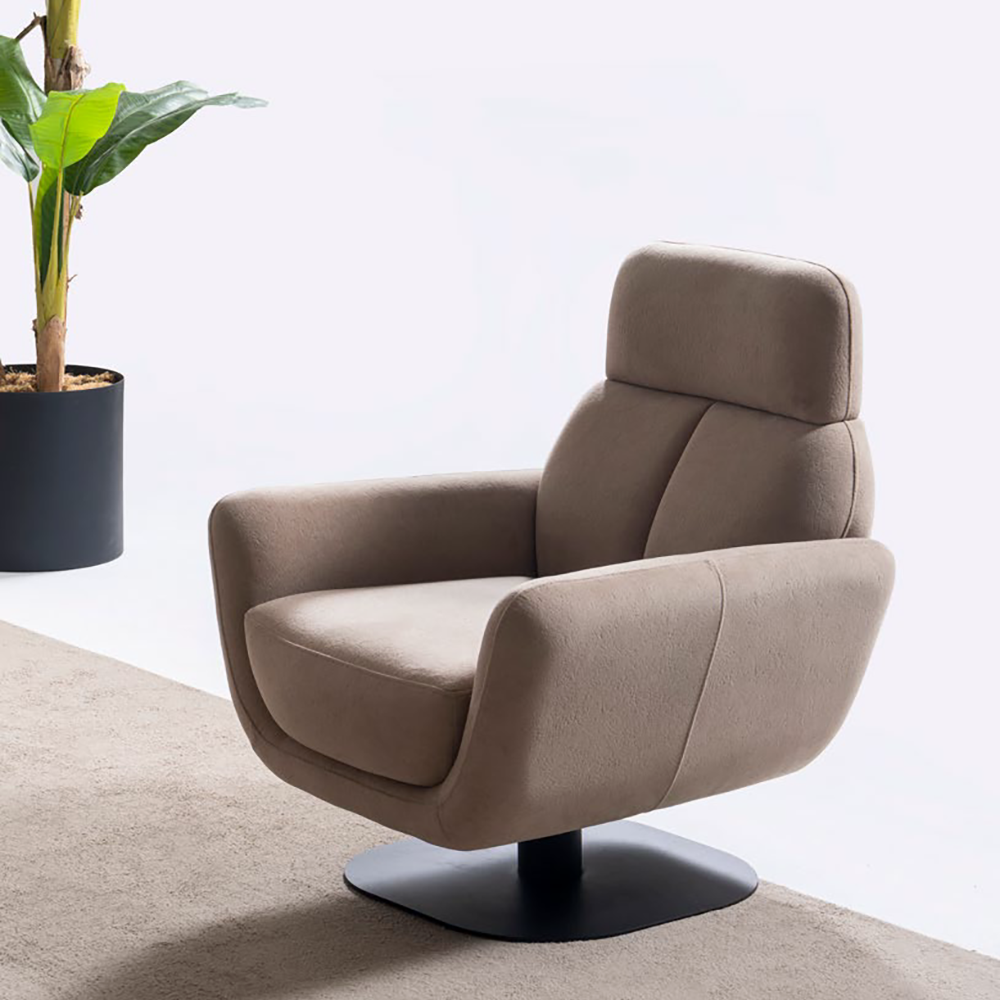 Beige upholstered swivel lounge chair on a black circular pedestal base beside a potted plant in a bright minimal room.