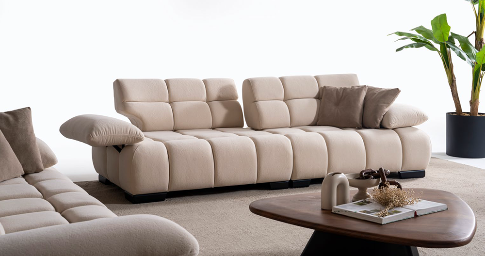 Liberta Living Room 5 Armonna Creamy beige modular sofa with plump cushions and matching pillows in a bright living room with a wooden coffee table and a tall potted plant nearby