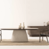 Minimalist dining room with an oval table on a rounded pedestal base two dark chairs and a sideboard