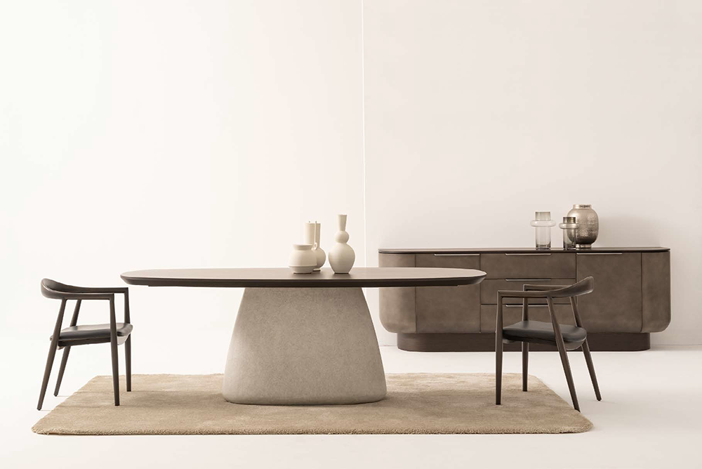 Minimalist dining room with an oval table on a rounded pedestal base, two dark chairs, and a sideboard.
