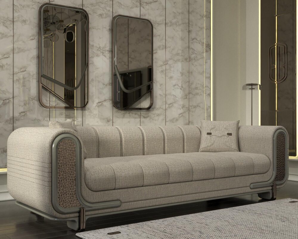 Luxurious beige fabric sofa with rounded tubular metal arms in a marble-walled living room, flanked by vertical gold-accent mirrors and a tall potted plant on the left, with a light rug in the foreground.