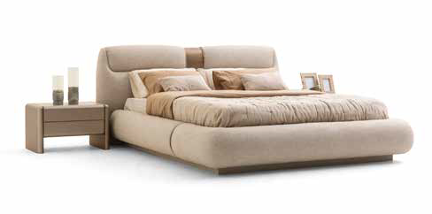 Beige upholstered bed with a padded headboard and matching nightstand, topped with decorative items and pillows.