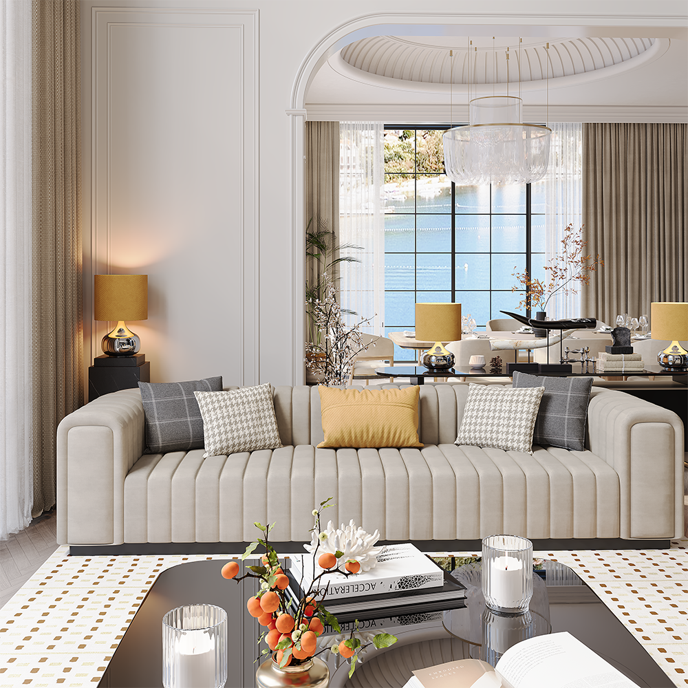 Luxurious living room with a beige, pleated sofa and gold-accent cushions facing a glass coffee table and candle decor, dining area in background.