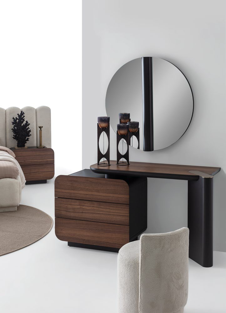 Modern bedroom vanity setup with a round mirror, dark wood drawers, and decorative candle holders on the surface.