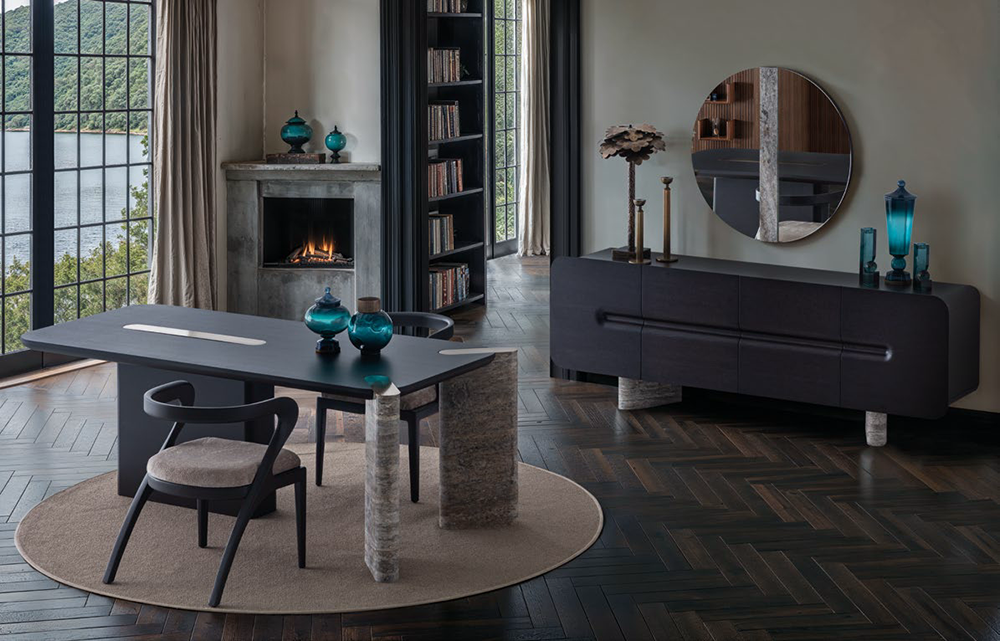 Modern dining room with a long black table, black chair, circular rug, and turquoise glass vases overlooking a lake view through large windows.