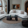 Bright modern living room with two white curved sofas around a black oval coffee table on a circular beige rug by a lit fireplace