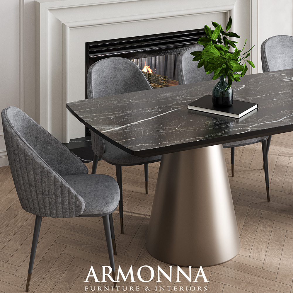 Dark marble dining table on a gold pedestal base with gray upholstered chairs; fireplace and a vase with greenery on the table in a stylish dining room.