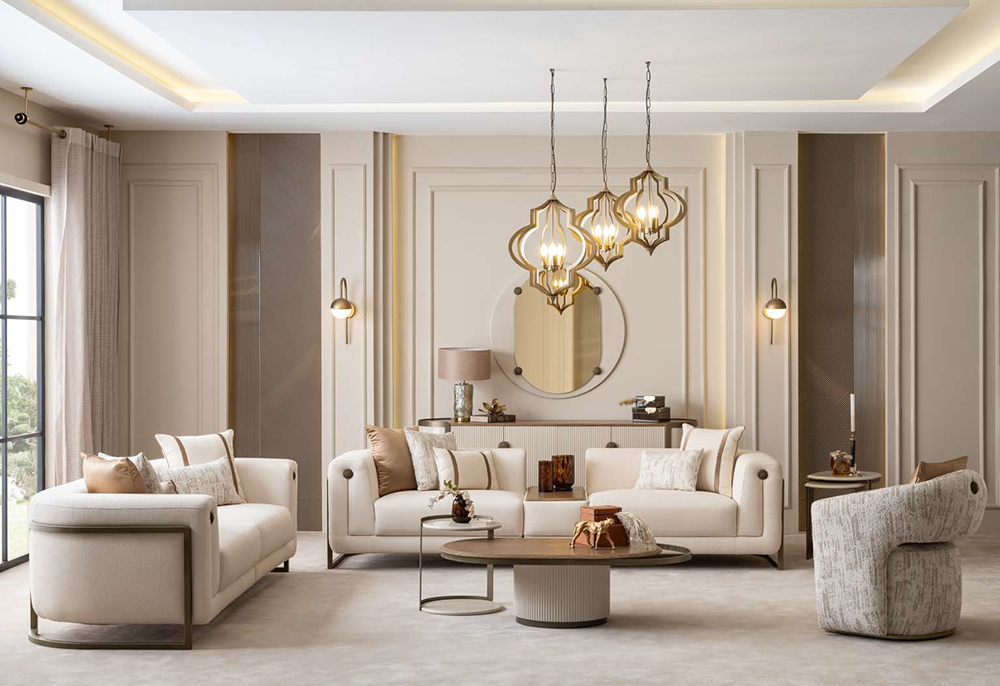 Elegant neutral living room with cream sofas, round mirror, and gold pendant lights over a coffee table. Large windows on the left bring natural light.