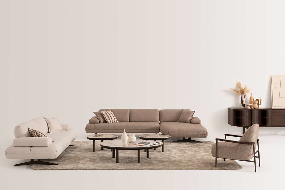 Modern beige living room with a sectional sofa, matching lounge chair, and round coffee tables on a light rug.
