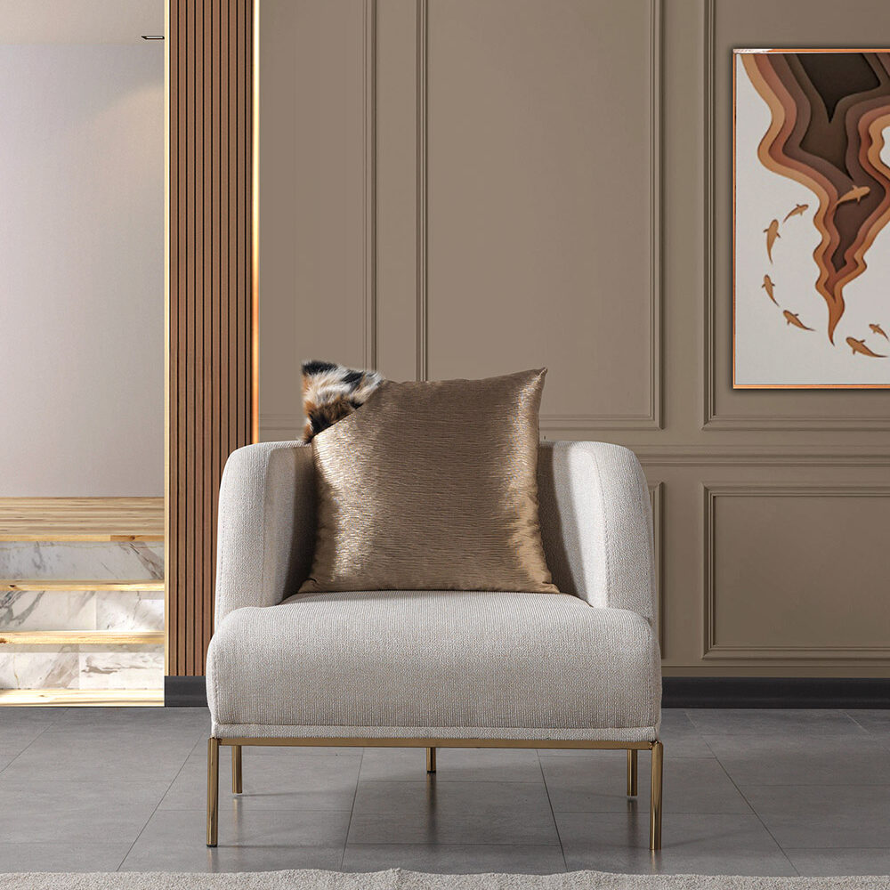 Gray upholstered armchair with a bronze metallic pillow in a beige-paneled living room, with a framed abstract artwork on the wall.