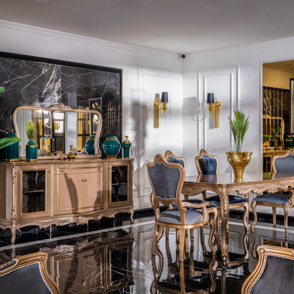 Luxurious dining room with gold-accented furniture, blue-upholstered chairs, teal vases, and a carved table set against a black marble wall.