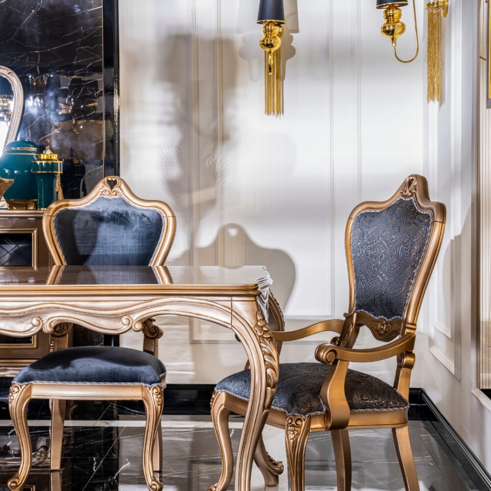 Luxurious dining room with a gold-trimmed carved table and blue upholstered chairs, black marble floor, and gold wall sconces on cream walls.