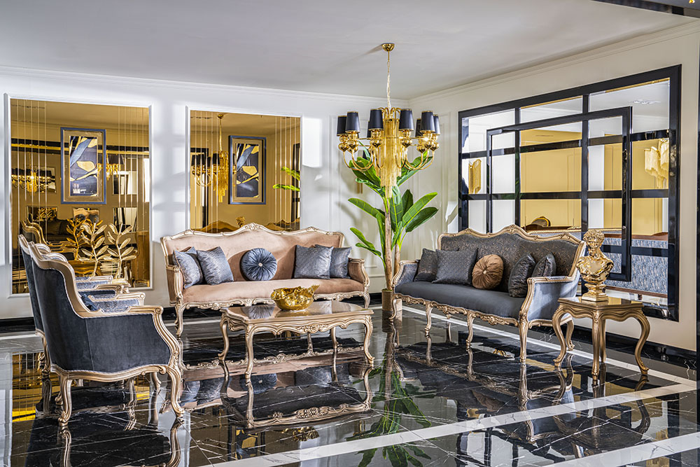 Luxurious living room with ornate gold-framed sofas, blue and blush cushions, and a gold chandelier on a black marble floor.
