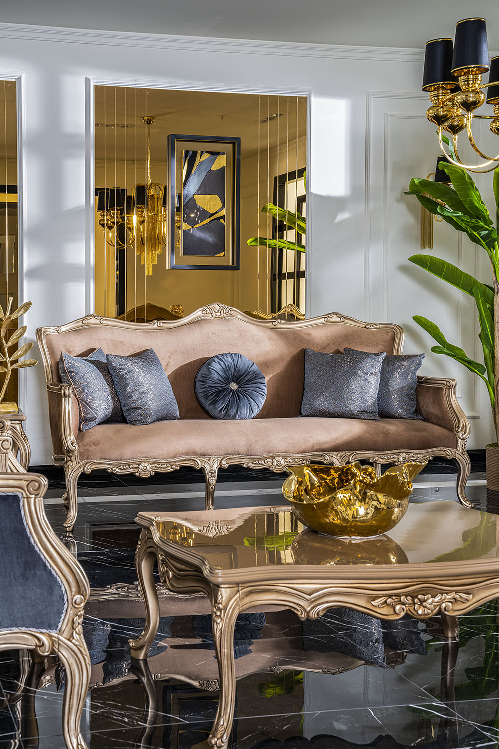 Napoli Classic Set 7 Armonna Elegant living room with a gold framed sofa matching ornate coffee table blue gray cushions and a gold bowl centerpiece set on a black and white tiled floor with chandeliers and a large green plant