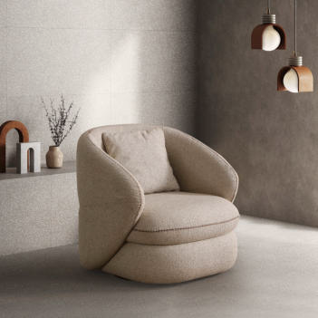 Beige circular lounge chair with curved arms in a minimalist living space with concrete walls and pendant lights.