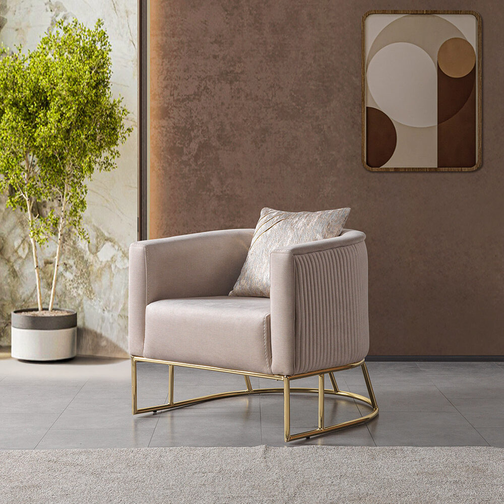Beige upholstered armchair with a gold metal base in a modern living room, next to a potted plant and abstract wall art.
