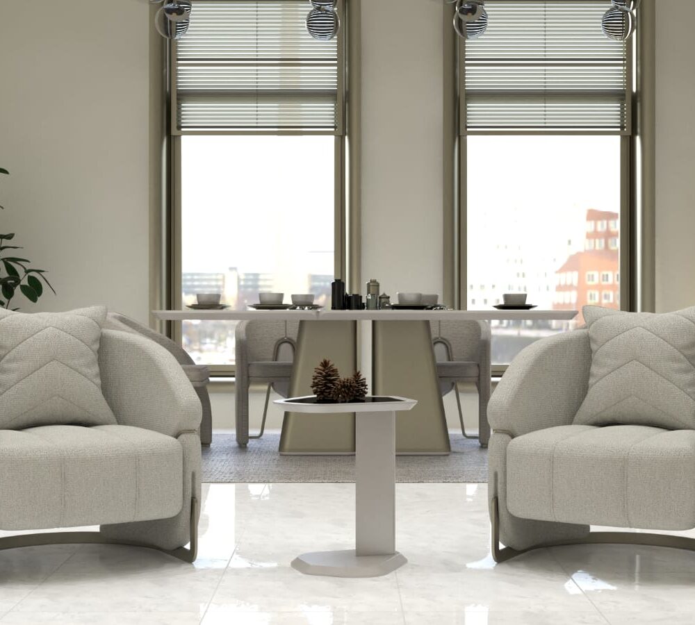 Bright modern living area with two plush beige armchairs facing a small round table between them, pinecones on top, and a dining table with place settings in the background near large windows.