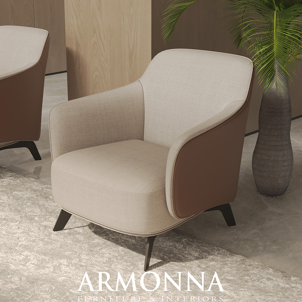 Beige and brown upholstered accent chair with curved arms in a modern showroom, ARMONNA Furniture & Interiors logo visible.