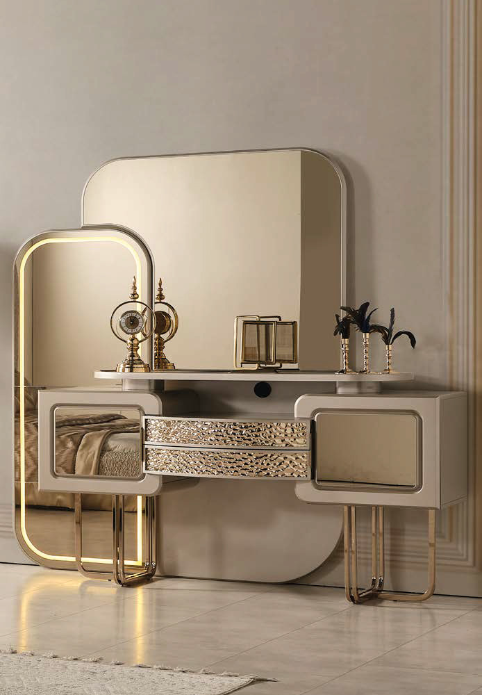 Luxurious beige vanity with a large rounded gold mirror, glass-topped surface, and gold-trimmed drawers with decorative accents on top of the dresser.