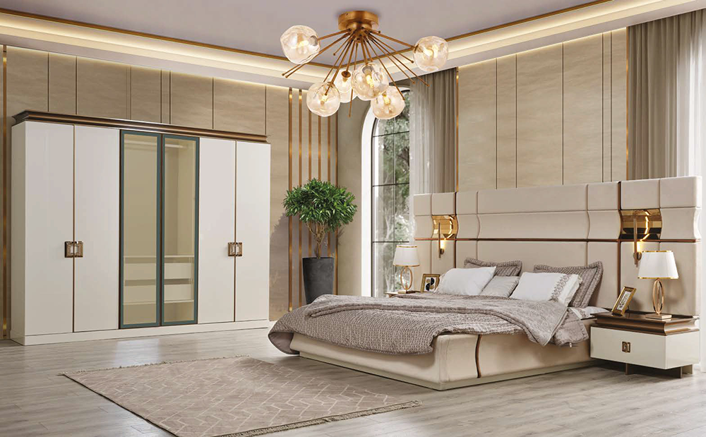 Luxurious modern bedroom featuring a large upholstered bed with matching headboard, two nightstands, and a gold-accent chandelier above. A tall wardrobe, potted plant, and large window with sheer curtains anchor the space.
