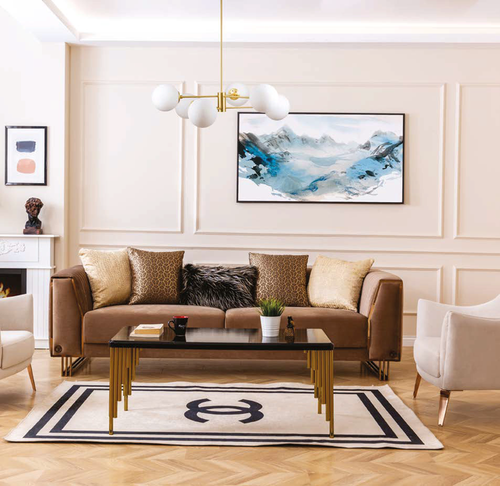 Cozy modern living room with a tan sofa gold accents and a glass coffee table in front of a framed blue mountain artwork