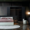 Luxurious dark bedroom with a low profile white bed and mauve bedding on a circular white rug flanked by black built in wardrobes