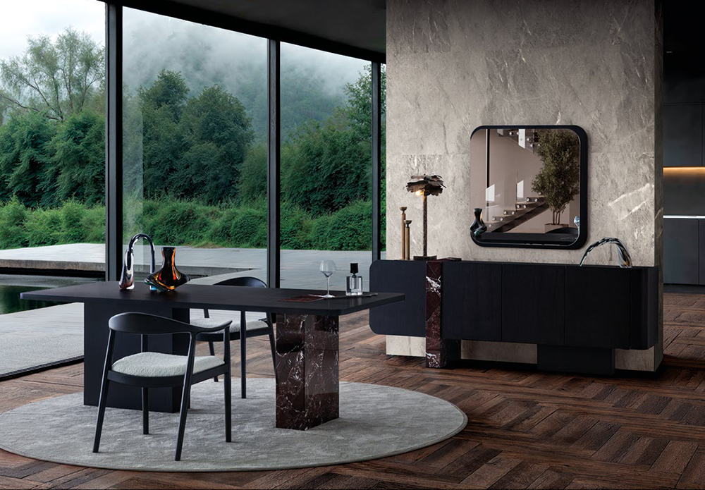 Contemporary dining area with a dark table and chairs on a round gray rug, marble pedestal base, and floor-to-ceiling windows overlooking greenery.